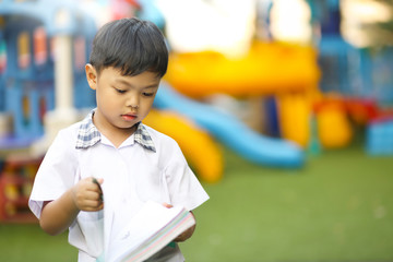 A little Asian boy reading a book in a school.