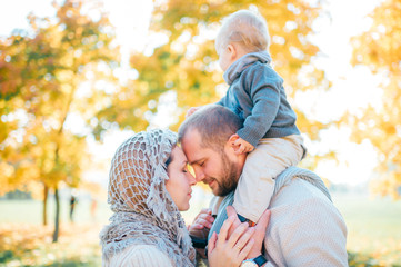 Family couple kissing outdoor with their baby sitting on fathers shoulders