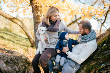 Happy family couple with their son and little puppy in autumn park