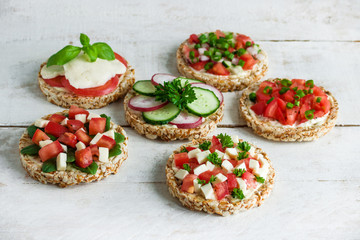 rice crisp cracker with chopped vegetables tomato cucumber radish parsley soft cheese on white...