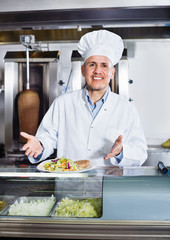 Cheerful mature man cook serving fresh kebab dish on plate