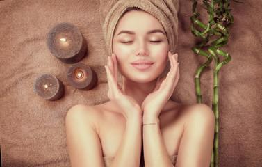 Beautiful spa woman with a towel on her head lying and touching face skin. Skincare. Beauty smiling...