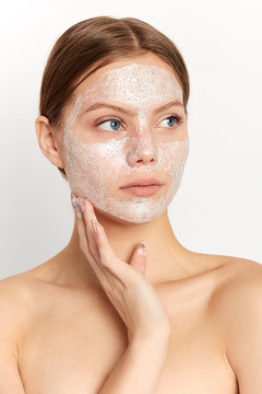 serious attractive girl has applyed scrub mask on face. close up portrait, girl with a plam on her cheek looking aside