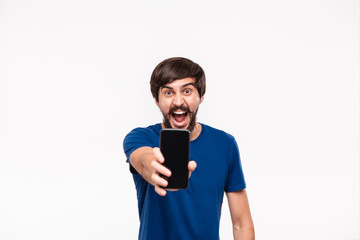 Good looking brunet man in a blue shirt with beard and moustaches showing smartphone screen at the camera standing isolated over white background.