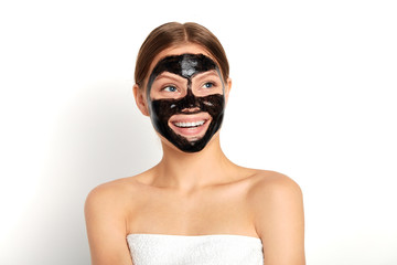 happy attractive young woman with nude shoulders using a black face mask, isolated white background, studio shot, beauty, skin, face care