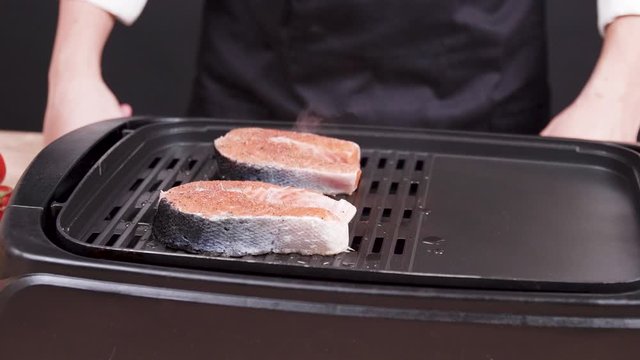 Chef supervising a fresh filett of salmon frying in a frying pan seasoned with salt and mediterranean herbs.