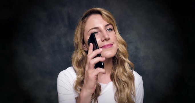 Attractive blonde speaks by a mobile phone on a dark background. 4K video.
