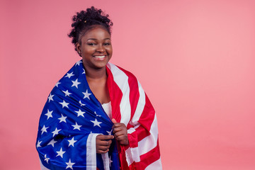 Smiling afro american woman holding USA flag and looking at camera in studio pink background