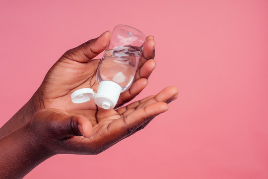 Close Up Hands Of Dark Skinned Woman Applying Alcohol Gel In Hand Pink Studio Background