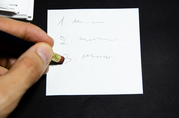 White square stickers crumpled pieces of paper of the same size on a black background with a simple pencil in a male hand