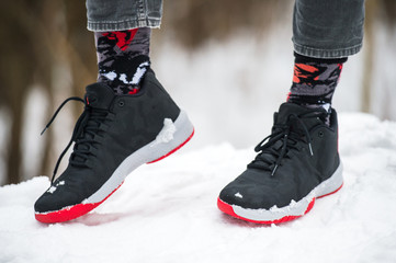 Male legs in athletic shoes, cropped jeans and fashionable socks standing on snow.  Stylish and trendy winter look.