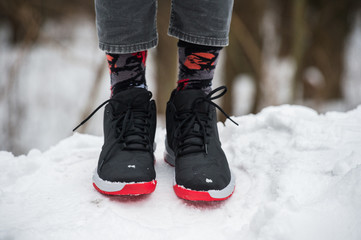 Male legs in athletic shoes, cropped jeans and fashionable socks standing on snow.  Stylish and trendy winter look.