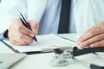 Mid section of male doctor writing write prescription to patient at worktable. Panacea and life save, prescribing treatment.