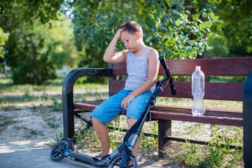 teenage boy sitting with a scooter on the bench . Boy rides in the Park, and happily smiling resting