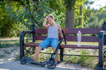teenage boy sitting with a scooter on the bench . Boy rides in the Park, and happily smiling resting