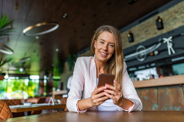 Portrait of young businesswoman use mobile phone while sitting in comfortable coffee shop during work break. Young woman in a cafe reading a text message from her mobile phone.