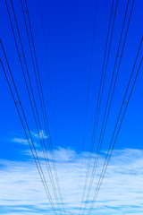 Electricity powerlines against a blue sky with light white clouds