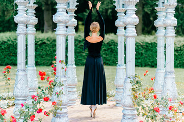 Young ballerina in black old fashioned dress posing in the arch at nature