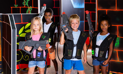 Joyful teens aiming laser guns at other players during lasertag game in dark room