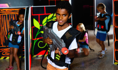Fototapeta na wymiar Portrait of tweenager boy with laser gun having fun on dark lasertag arena