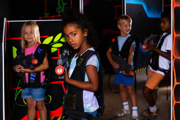 Teenager girl with laser pistol posing in laser tag labyrinth