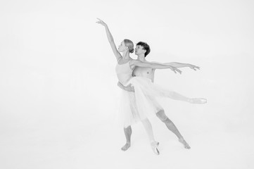 Young couple of modern ballet dancers posing over white studio background