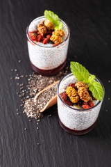 Healthy food concept Chia seeds, milk pudding with goji, white mulberry and mix dried seeds in small Glass on black slate board background