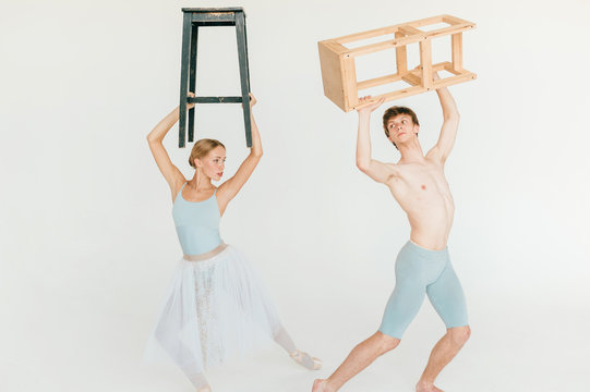 Funny and unusual couple of modern ballet dancers posing with chair in hands above their heads