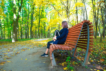 Fototapeta premium girl sits on a bench in the autumn park