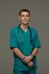 Attractive young doctor man posing with folded arms isolated on a grey background.