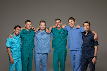 Successful team of medical doctors are looking at camera and smiling while standing on gray background.