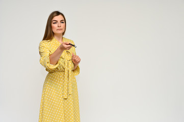 Obraz premium Portrait of a cute middle-aged manager brunette woman with beautiful curly hair in a yellow dress on a white background with a pen in her hands. Beauty, brightness, smile.