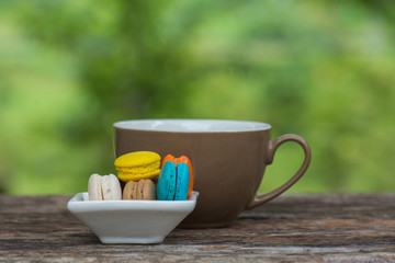 Cup of coffee and Colorful Macaroons in dish on wooden table