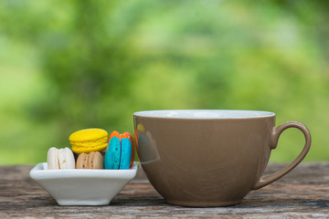 Cup of coffee and Colorful Macaroons in dish on wooden table