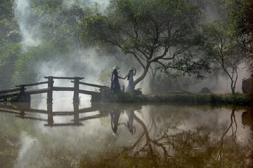 Obraz na płótnie Canvas Romantic Vietnamese landscape with lake, traditional bridge and two women dressed in traditional Vietnamese dress