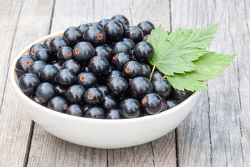 Ripe fresh black currants in a bowl on a wooden background
