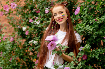 Cheerful lesbian with lgbt rainbow on her face posing in blooming flowers