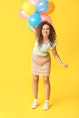 Fototapeta premium Happy African-American woman with air balloons on color background