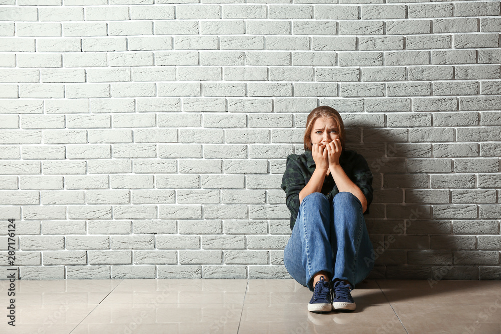 Wall mural Woman having panic attack while sitting near brick wall