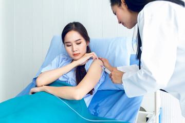 Asian young female doctor being injecting a young woman patient, who shows anxious facial expression and lying in bed In the room to treat the illness better.