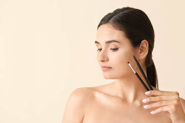 Young woman correcting her eyebrows on light background