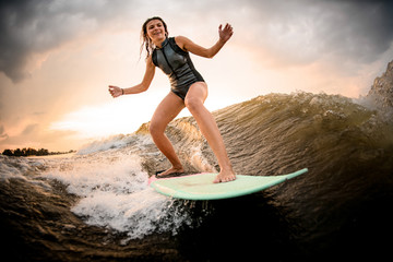 Slim fit girl riding on the wakeboard on the river on the wave on the bending knees