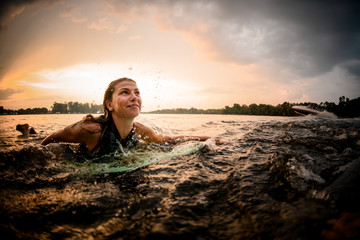 Sporty girl swimming lying on the wakeboard on the river on the wave