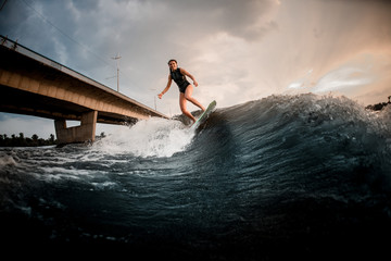 Beautiful girl riding on the wakeboard on the river in the background of the bridge