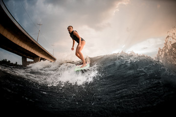 Sporty girl standing on the wakeboard on the river in the background of the bridge