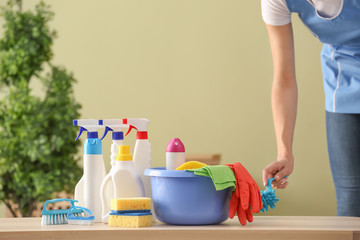 Female janitor with cleaning supplies on table in room