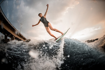 Girl riding on the wakeboard on the river in the background of the bridge rising hands