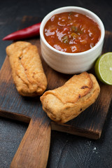 Brazilian empanadas with salsa sauce on a rustic wooden chopping board, vertical shot, close-up