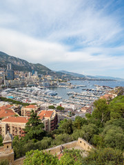 Fototapeta premium Monaco, july 2019: Monte Carlo cityscape. Real estate architecture on mountain hill background. Many high-rise buildings in downtown area. Yachts moored at town in sunny summer Day