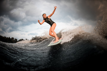 Young girl riding on the wakeboard on the river in the background of trees rising hands